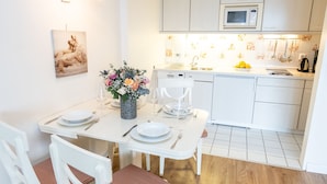 A modern kitchen with white cabinetry, a microwave, and a sink. There is a dining table set with plates, cutlery, and a vase of flowers. - Bright and cozy vacation apartment directly on the beach crossing in Westerland (Westerland)
