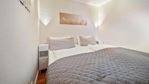 A bedroom with a large bed, two bedside tables, a nightstand, a wall-mounted lamp, and a painting. - Bright and cozy vacation apartment directly on the beach crossing in Westerland (Westerland)