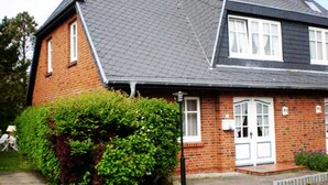 A two-story brick house with a dark roof, white-framed windows, and a front door with a small porch. - 3-room apartment on the ground floor in a quiet location in Alt-Westerland (Westerland)