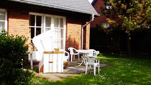 A house with a brick exterior, a covered porch with white plastic chairs, and a small garden area. - 3-room apartment on the ground floor in a quiet location in Alt-Westerland (Westerland)