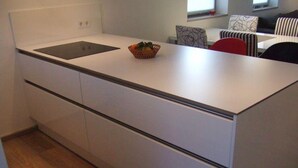 A modern kitchen with white cabinetry, a black countertop, and a small fruit bowl. - Spacious 3-room apartment with terrace and garden in Wenningstedt (Wenningstedt)