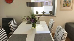 A dining area with a white table, striped chairs, a vase with flowers, a starfish decoration, and a clock on the wall. - Spacious 3-room apartment with terrace and garden in Wenningstedt (Wenningstedt)