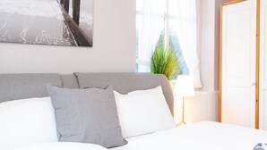 Ein Schlafzimmer mit Bett, Kissen, einem Nachttisch mit Lampe, einem Fenster mit Vorhängen und einer Tür.