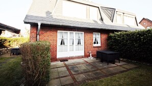 Ein zweigeschossiges Haus mit geneigtem Dach und einer Ziegelaußenfassade. Vor dem Haus befindet sich eine kleine Terrasse mit Gartenmöbeln.