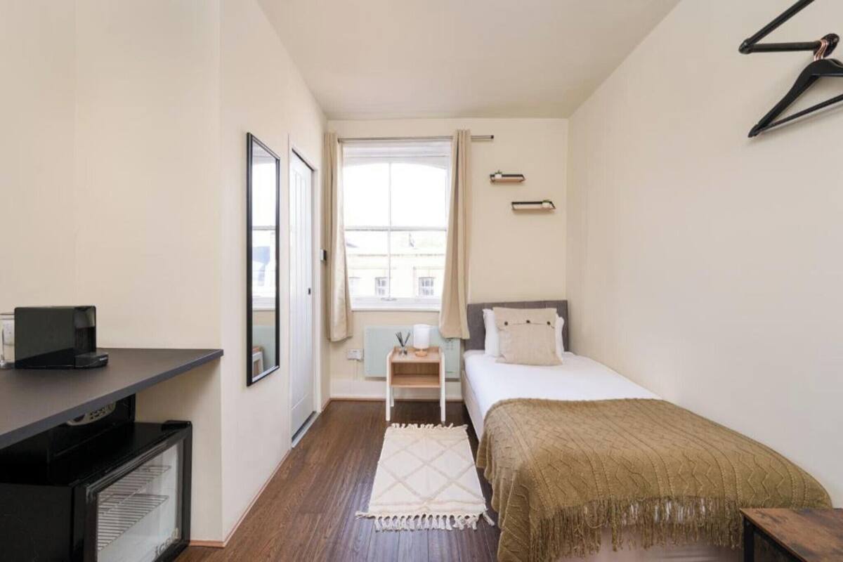 A compact bedroom with a bed, bedside table, and a small desk with a computer.