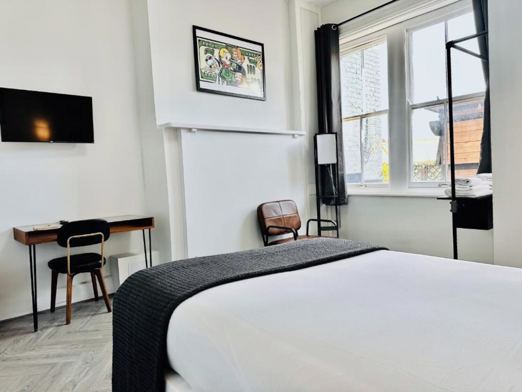 A hotel room with a bed, a desk, a chair, a TV, and a window with curtains.