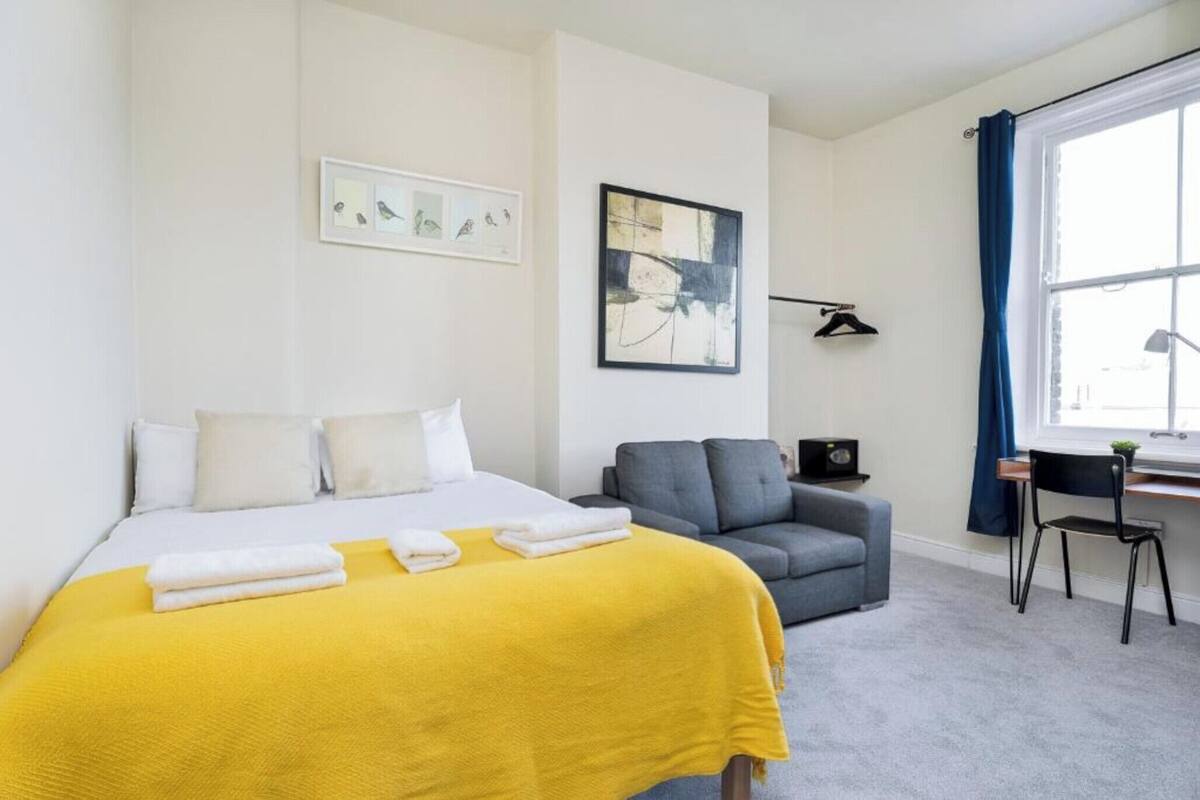 A hotel room with a bed, a sofa, a desk, and a window with curtains.