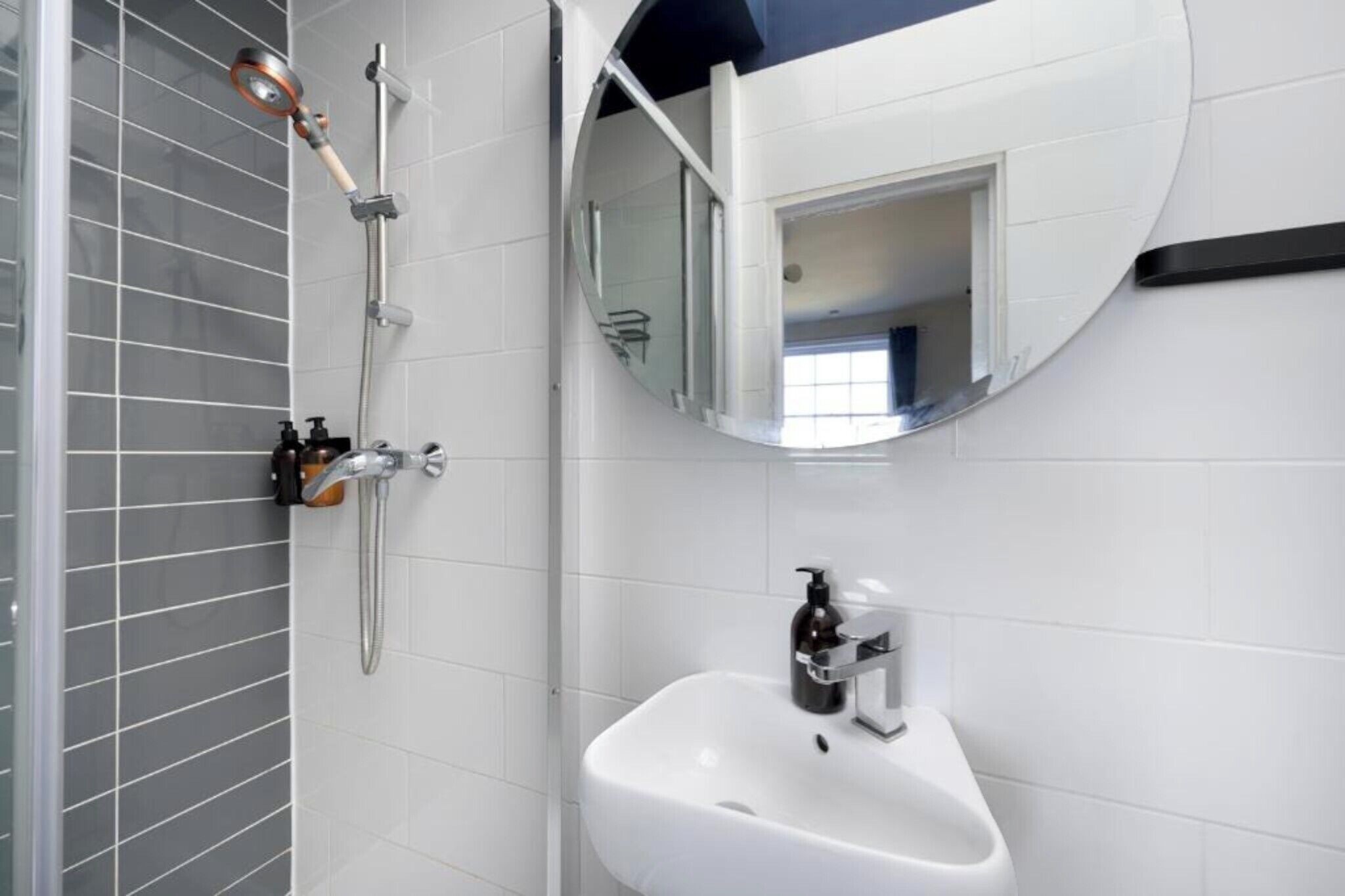 A modern bathroom with a white sink, a handheld showerhead, and a mirror with a built-in light.