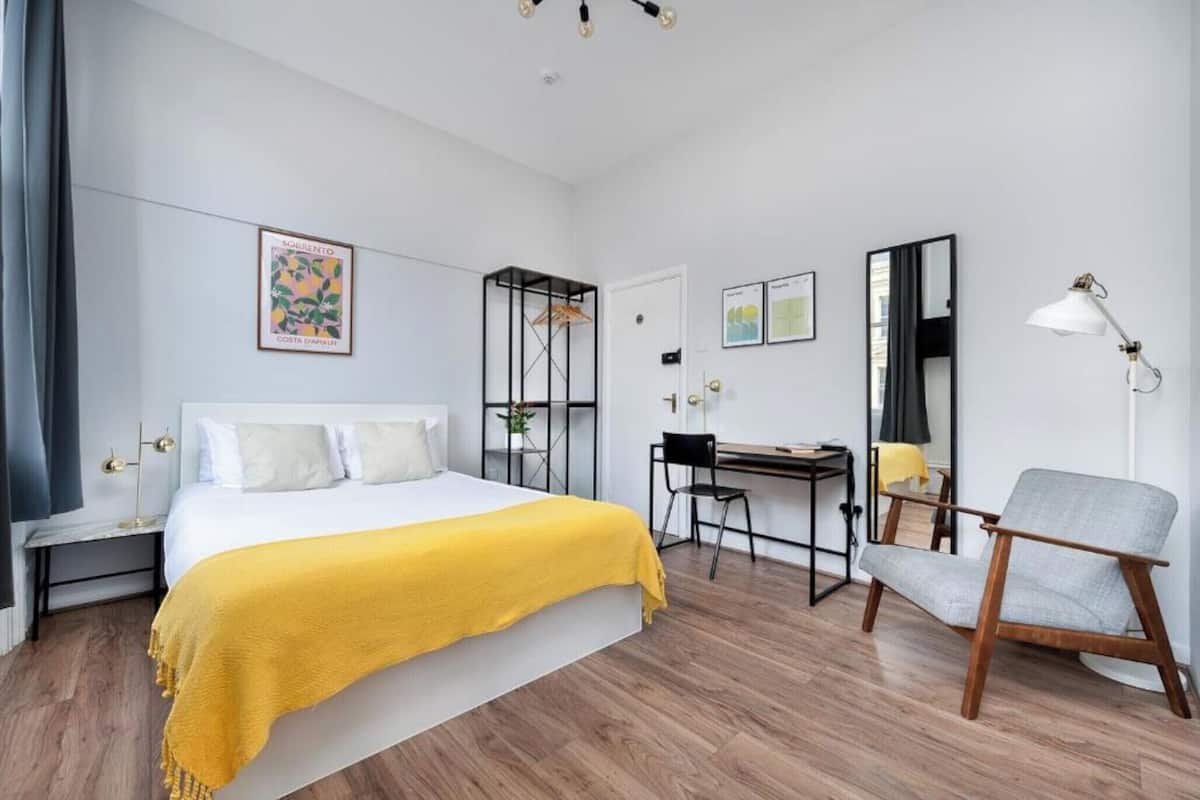 A bedroom with a bed, a desk, a chair, and a mirror.