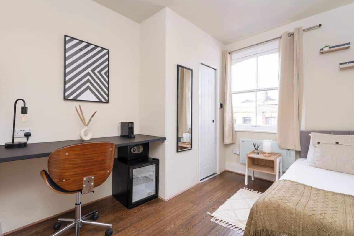 A modern bedroom with a bed, desk, chair, and a large window.