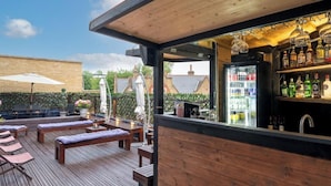 Une terrasse en bois avec des chaises longues et un coin bar équipé d’un réfrigérateur et d’étagères remplies de bouteilles.