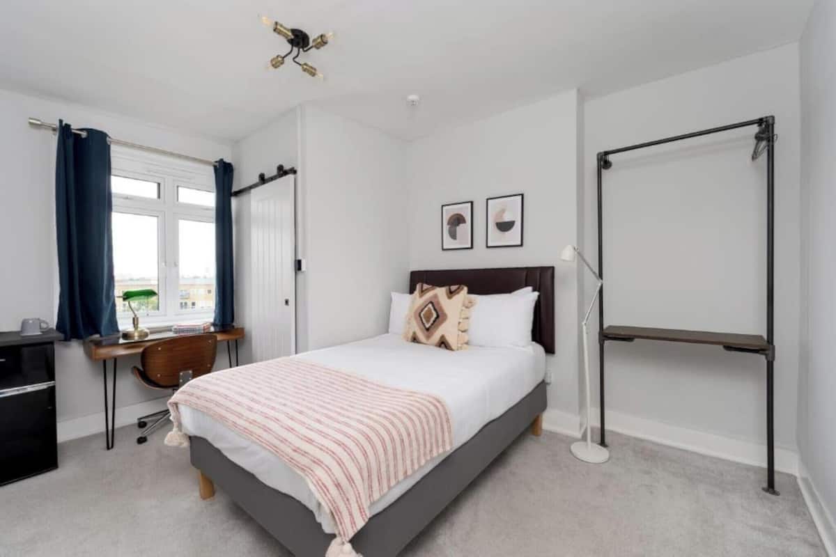 A bedroom with a bed, a desk, a chair, a wardrobe, and a window with curtains.