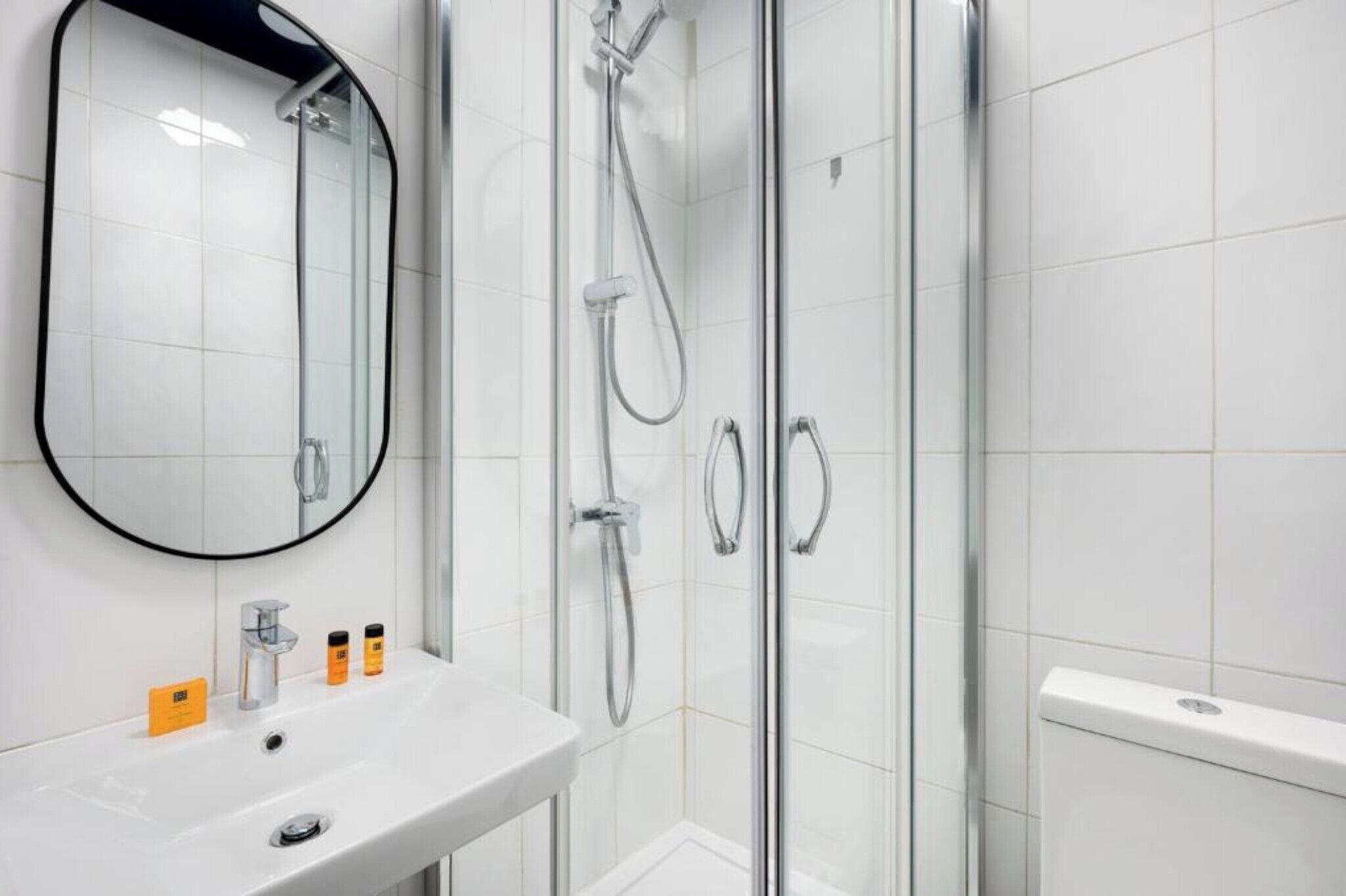 A modern bathroom with a glass shower enclosure, a white sink with a mirror, and toiletries.