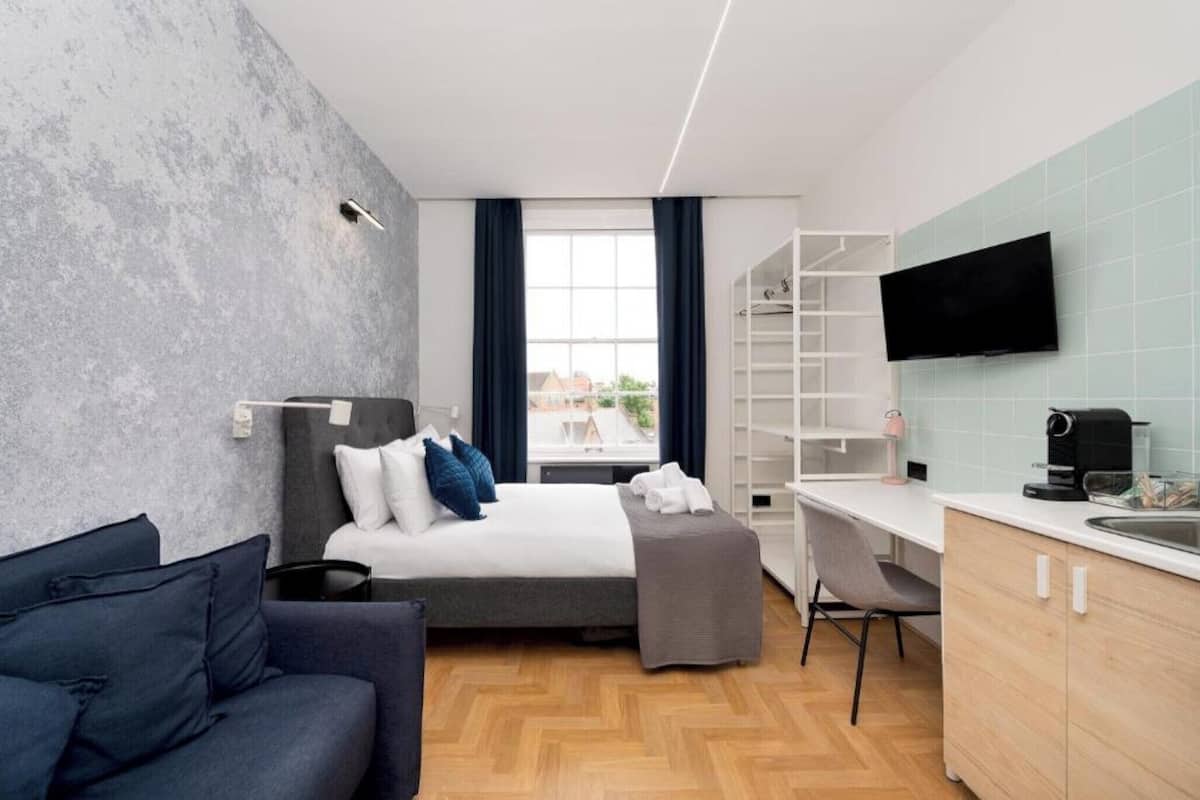 A modern hotel room with a bed, a desk, a sofa, a TV, and a window with curtains.