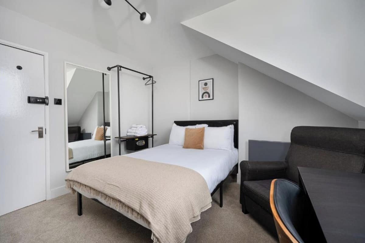 A modern hotel room with a bed, a chair, a desk, and a large mirror.