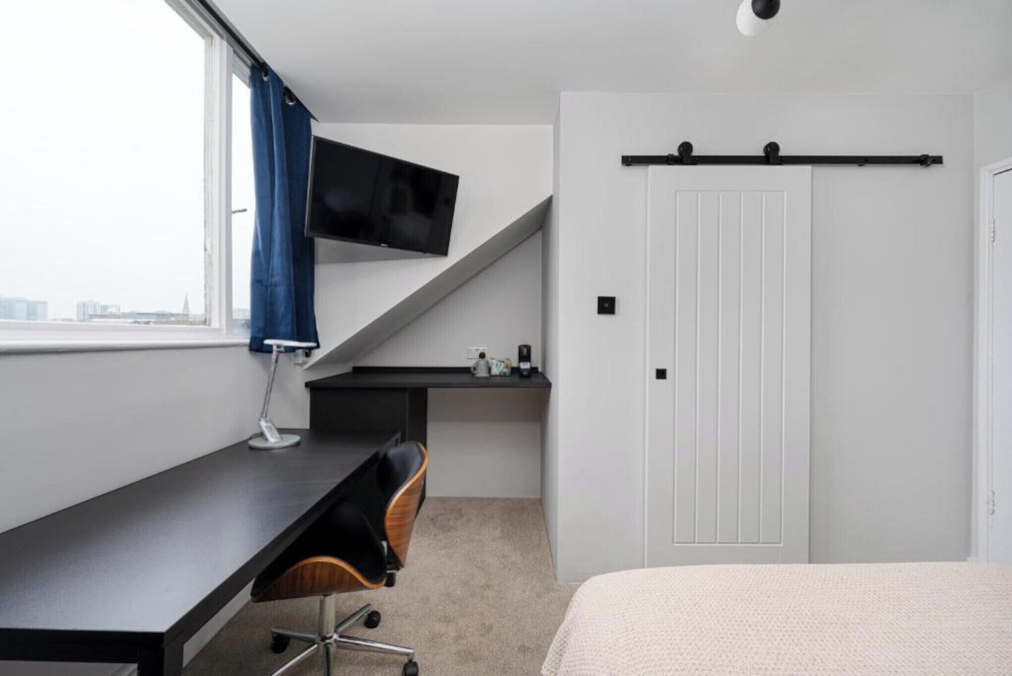 Une chambre avec un bureau, un lit, un téléviseur fixé au mur et une porte de placard coulissante.