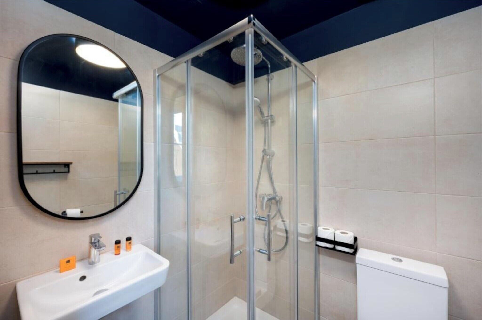 Un baño moderno con ducha envuelta en cristal, un lavamanos blanco con artículos de aseo y un inodoro.
