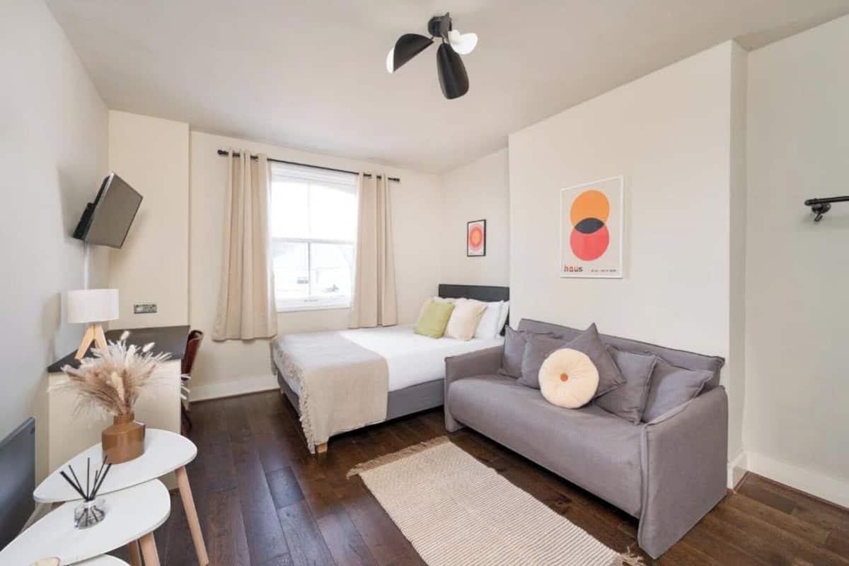 A compact hotel room with a bed, a sofa, a small table, and a TV mounted on the wall.