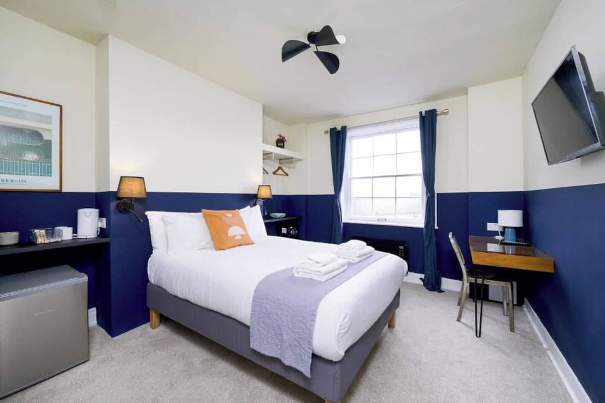 A neatly arranged hotel room with a bed, bedside tables, a desk, a chair, a TV, and a window with curtains.