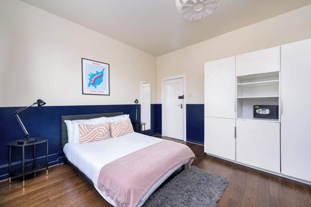 A bedroom with a bed, a nightstand, a desk lamp, a wardrobe, and a framed map on the wall.