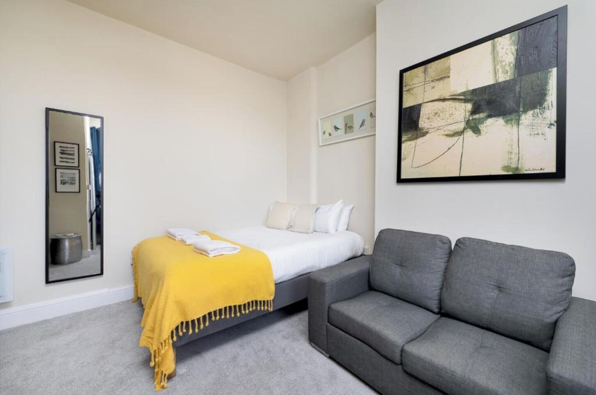 Et moderne hotelværelse med en seng, en sofa, et indrammet abstrakt maleri og et spejl.
