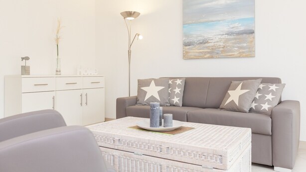Un salon moderne avec un canapé gris, des coussins à motifs étoilés, un meuble blanc et un tableau représentant un paysage.
