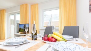 Une table à manger dressée avec des assiettes, des couverts, des verres à vin et un saladier de fruits.