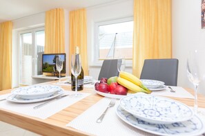 A dining table set with plates, cutlery, wine glasses, and a fruit bowl. - Cozy 2-room apartment on the ground floor in Westerland (Westerland)