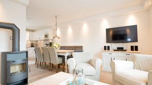 A modern living room with a fireplace, a dining area, and a TV mounted on the wall. - Modern vacation home with its own sauna, whirlpool bath and terrace (Tinnum)