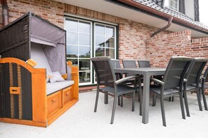 A patio with a wicker sofa, a table, and chairs. - Modern vacation home with its own sauna, whirlpool bath and terrace (Tinnum)