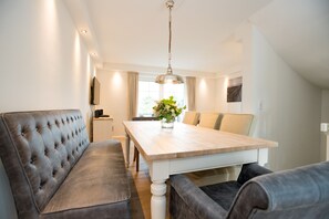 A modern dining area with a wooden table, cushioned bench seating, and a hanging light fixture. - Modern vacation home with its own sauna, whirlpool bath and terrace (Tinnum)