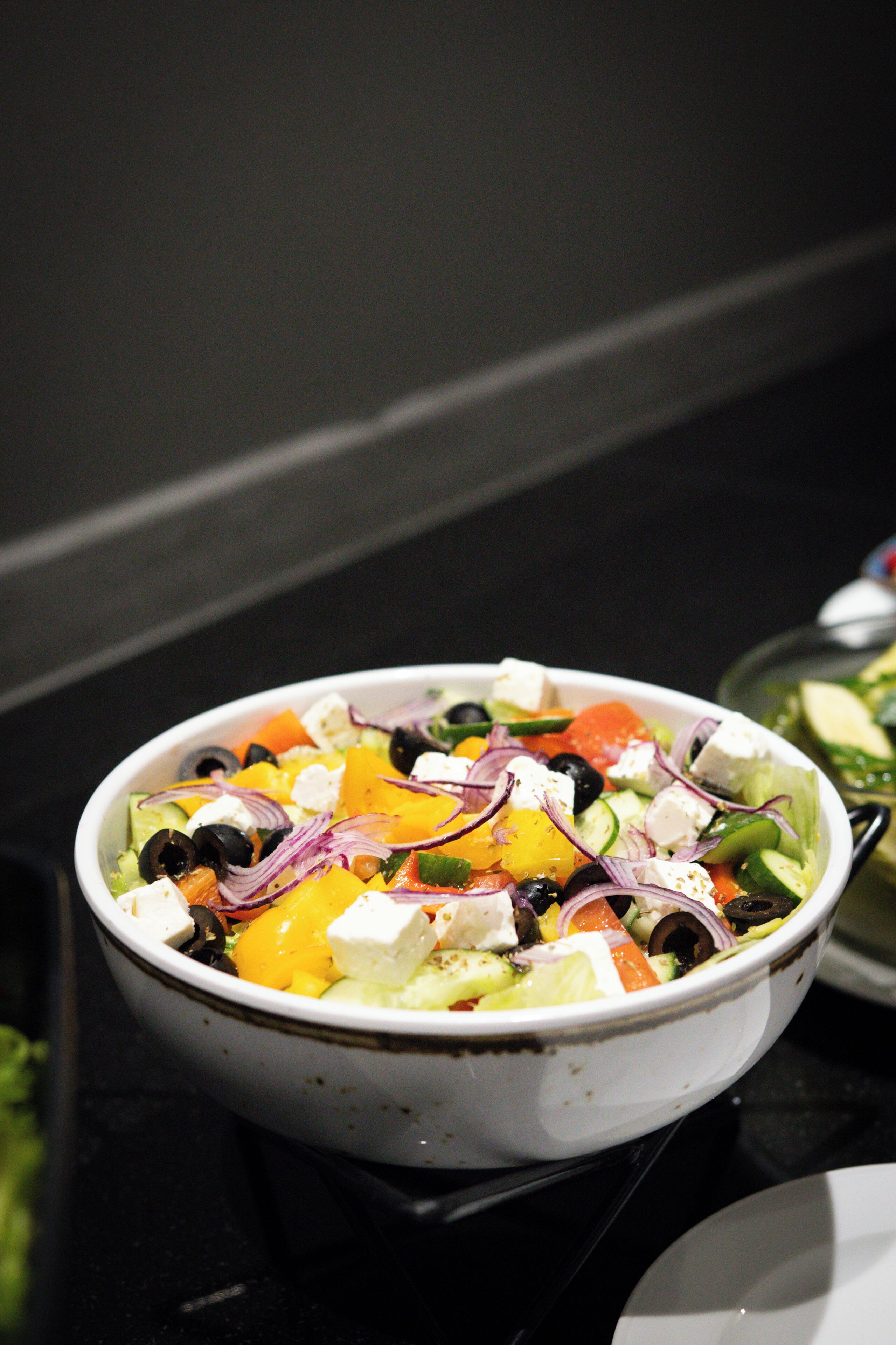 A bowl of salad with various vegetables and cheese on a table.