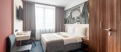 A hotel room with a bed, desk, chair, and a large window.