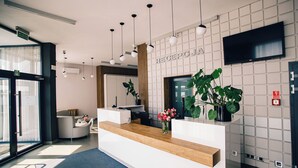 A modern reception desk with a wooden counter, a large mirror, and a reception area with a TV mounted on the wall. - Terminal Hotel (Wrocław)