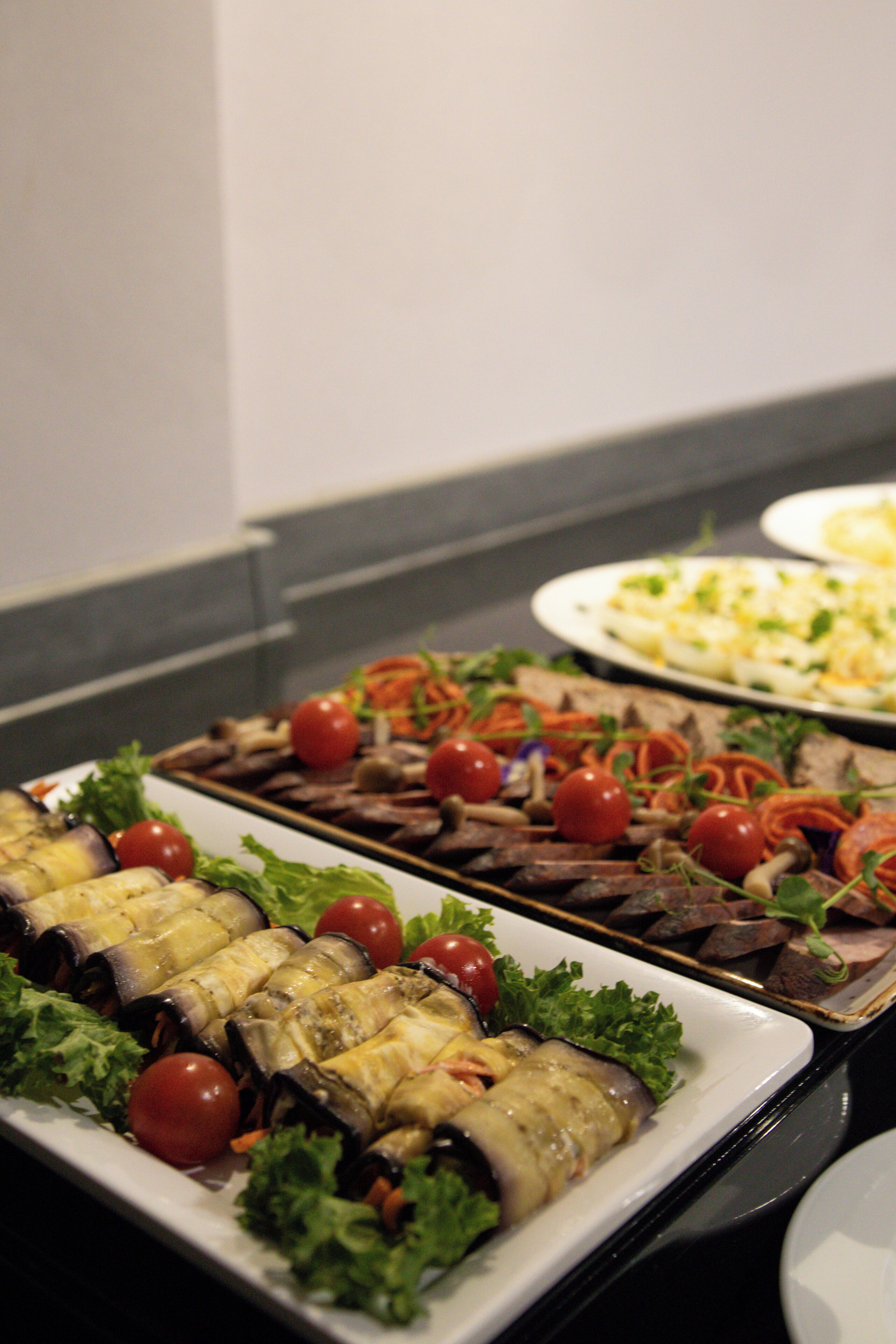 A buffet table with various dishes including vegetables and rolls.
