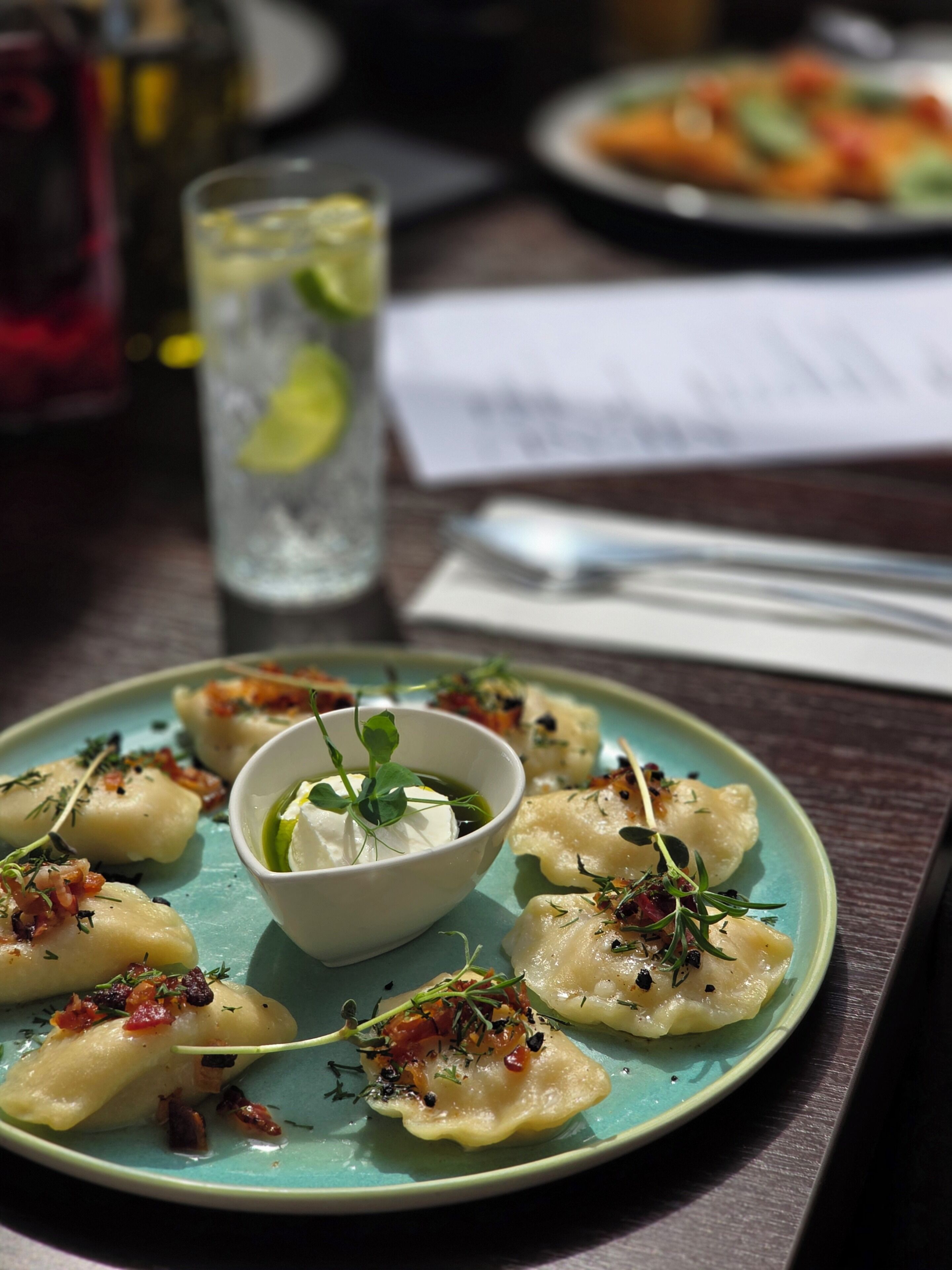 A plate of dumplings with a garnish, a glass of water, and a menu on a table.