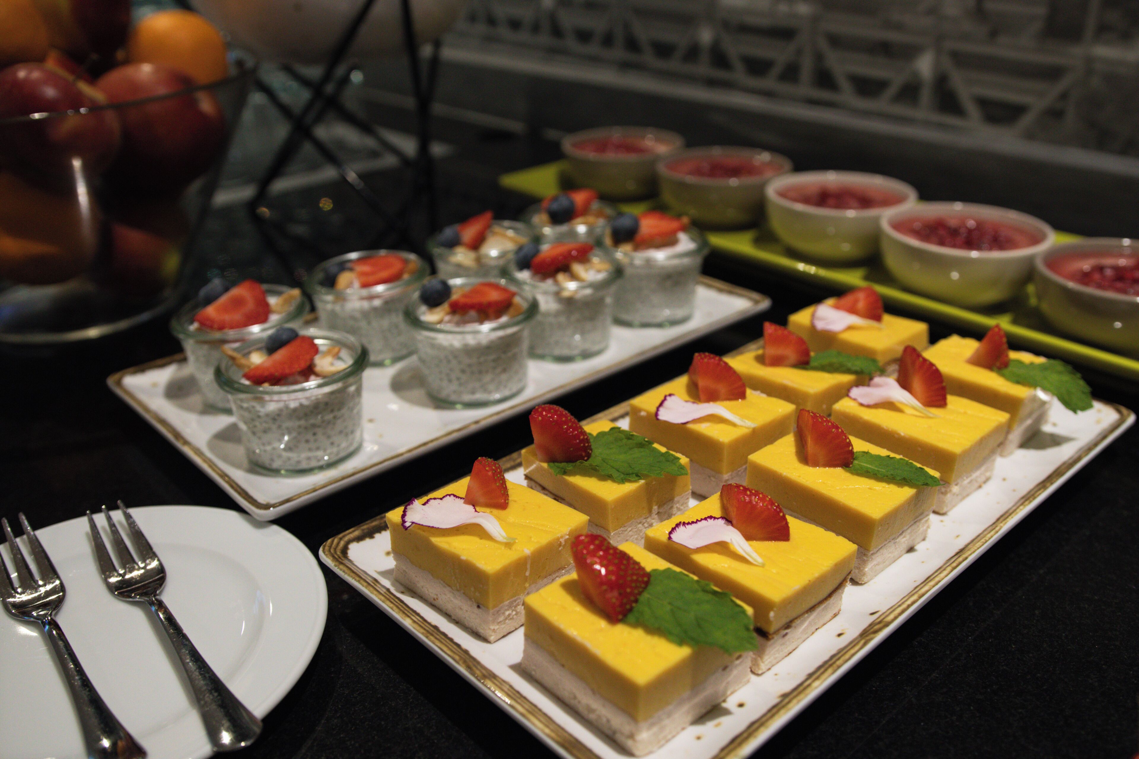 Un buffet proposant une variété de desserts, notamment des carrés de gâteau garnis de fruits et un dessert jaune à plusieurs couches.