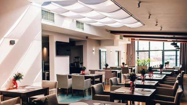 A modern restaurant with multiple dining tables, chairs, and potted plants. - Terminal Hotel (Wrocław)