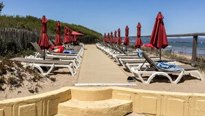 En strandpromenade med liggestole og røde parasoller, der fører hen til havet.
