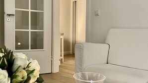 Ein Wohnzimmer mit einem weißen Sofa, einem Glaswindlicht auf einem Holztisch und einer Tür mit satinierten Glasscheiben.
