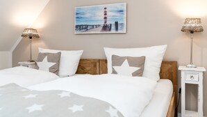 Ein Schlafzimmer mit einem Bett, zwei Nachttischen, einer Lampe und einem Bild eines Leuchtturms an der Wand.