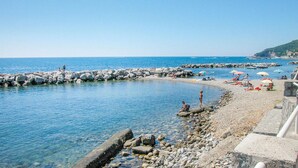 Una spiaggia rocciosa con acque cristalline azzurre, alcune persone che prendono il sole e ombrelloni.