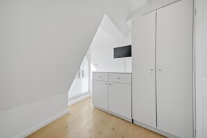 Ein modernes, helles Interieur mit schrägverdeckter Decke, Holzboden und integriertem Fernseher.