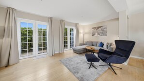 A spacious living room with a grey sofa, a dark armchair, a coffee table, and a large window with curtains. - Beautiful house Uter with terrace and modern furnishings in Westerland (Westerland)