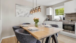 A modern kitchen with white cabinets, a built-in oven, and a dining area with a wooden table and grey chairs. - Beautiful house Uter with terrace and modern furnishings in Westerland (Westerland)