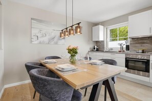 Eine moderne Küche mit weißen Schränken, einem eingebauten Ofen und einem Essbereich mit Holztisch und grauen Stühlen.