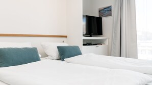 A hotel room with a bed, a television on a stand, and a window with curtains. - Modern vacation apartment with sauna and heated indoor pool in Westerland (Westerland)
