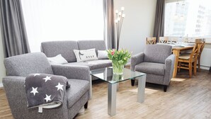 Uma sala de estar moderna com sofás cinza, uma mesa de centro de vidro e uma área de jantar com cadeiras e mesa de madeira.