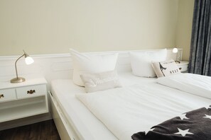 A neatly made bed with white bedding and a star-patterned blanket, a bedside lamp, and a nightstand with a lamp. - Modern & newly renovated vacation apartment, close to the center & beach (Westerland)