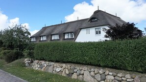 Ein traditionelles Haus mit einem Strohdach, weißen Wänden und einer Steinmauer davor.